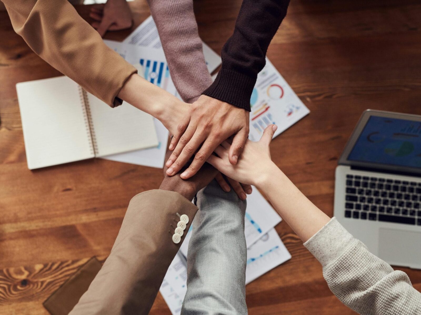 Hands stacked on top of each other from a diverse group of people in a huddle.